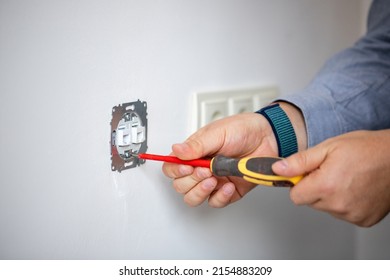 Man doing electrics. Close up of man installing electrical outlet in wall in room of house. Male electrician uses screwdriver to tighten bolts while attaching metal part of socket to wall. - Shutterstock ID 2154883209