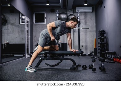 Man trainiert mit einer Hantel, die sich auf einer Sportbank im Fitnessraum befindet. Foto eines sexy muskulösen Mannes in Sportbekleidung und gute Physik auf grauem Hintergrund. Stärke und Motivation, Sport, Fitnessziel