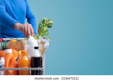 Man Doing Grocery Shopping At The Supermarket, He Is Putting A Milk Bottle In The Shopping Cart