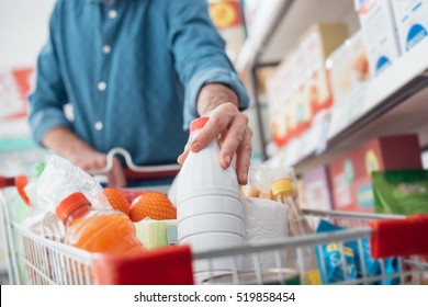 Man Doing Grocery Shopping At The Supermarket, He Is Putting A Bottle Of Milk In The Cart