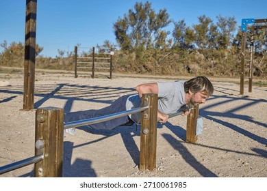 Man doing incline push-ups using metal bar at outdoor workout area.