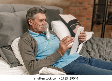 Man doing inhalation through oxygen mask at home bedroom and use laptop. - Shutterstock ID 1715429044