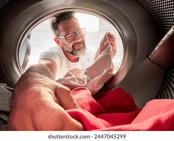 Man Doing Laundry Reaching Inside Washing Machine. One adult male washing clothes. View from inside the laundry. Homework husband. People using washing machine in laudromat - Powered by Shutterstock