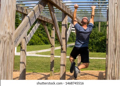 Man doing monkey bars on an obstacle course outside. - Powered by Shutterstock