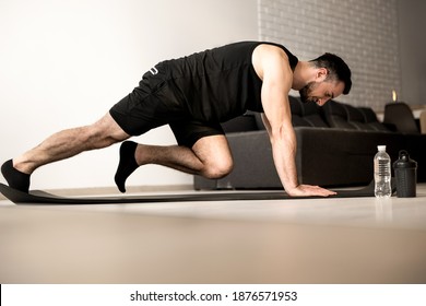 Man Doing Mountain Climber Exercises On Black Yoga Mat. Morning Workout. White Modern Living Room On Background. Plastic Bottle Of Water. Hard Workout. Training At Home.