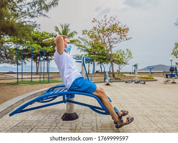 Man Doing Physical Exercises, Push Ups, Strength Exercises, Leans In Empty Outdoor Public City Park Metal Gym Wearing Mask Alone For Covid19 Prevention. Healthy Lifestyle In Quarantine And Coronavirus