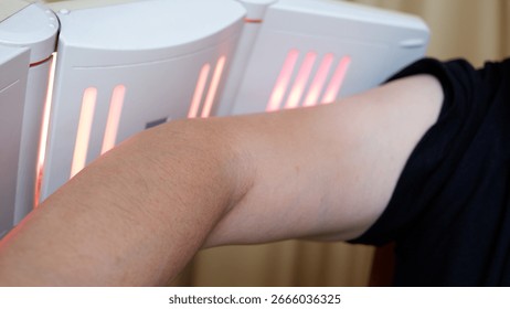 A man doing physiotherapy using an infrared lamp for arm.
