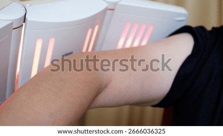 A man doing physiotherapy using an infrared lamp for arm.