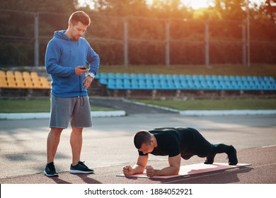 Man Doing Plank Exercise And Workout With Personal Fitness Trainer Outdoor