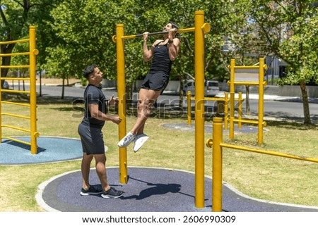 Man doing pull-ups in a park while his trainer watches him