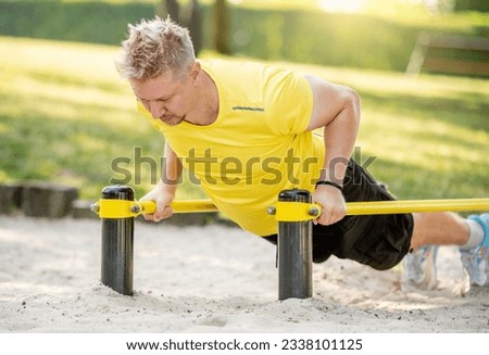 Man doing push ups with horizontal bar outdoors in park for healthy wellbeing. Sportsman guy making strong workout for muscle