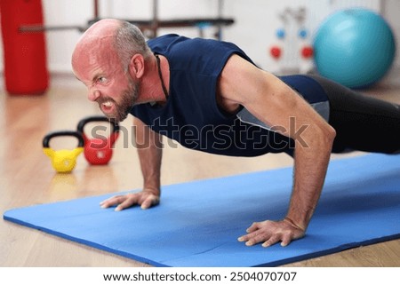Man doing push-ups on blue mat in gym, very strenuous