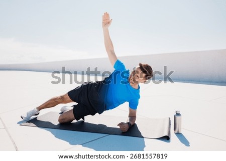 Man doing side plank exercise on rooftop with water bottle nearby