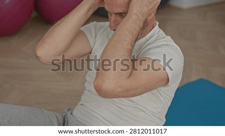Man doing situp with hands on head on blue mat in studio beside exercise balls; wellness determination.