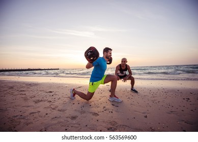 Man doing squats with his life coach at sunrise beach. 