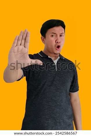a man doing stop sing with palm of the hand. warning expression serious gesture on the face. Portrait of serious young Asian man showing stop gesture, demonstrating denial sign, rejecting sign.