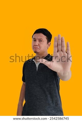 a man doing stop sing with palm of the hand. warning expression serious gesture on the face. Portrait of serious young Asian man showing stop gesture, demonstrating denial sign, rejecting sign.