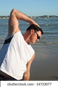 Man doing stretching exercises on the beach just after sunrise.