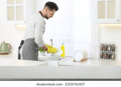 Man doing washing up in kitchen, focus on empty grey stone table - Shutterstock ID 2310741457