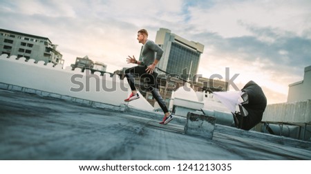Man doing workout using resistance parachute on rooftop. Side view of a fitness man running with a resistance parachute on terrace of a building.