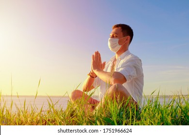 Man Doing Yoga Sitting In A Lotus Pose Wearing PPE Face Mask. Workout Outdoors Post Quarantine. Coping With Panic, Anxiety, Global Pandemic. Safety Measures Covid-19. New Crisis Regulations Reality.