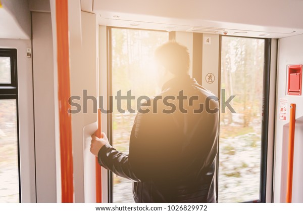 A man at the door of a train is talking on the phone\
during a trip