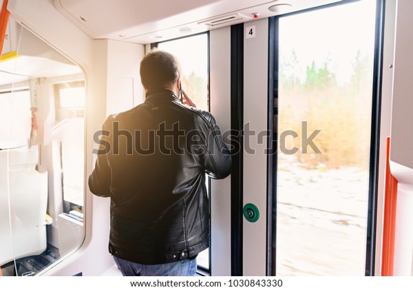 A man at the door of a train is talking on the phone\
during a trip