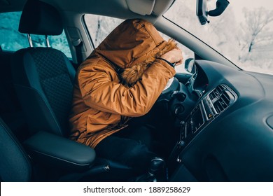 Man In Down Jacket Tries To Keep Warm And Not Freeze In His Stalled Car In Winter. The Concept Of A Dangerous Accident Or Heater Failure In The Cold Season