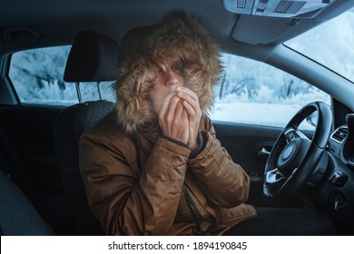 Man in down jacket tries to keep warm and not freeze in his stalled car in winter. The concept of a dangerous accident or heater failure in the cold season