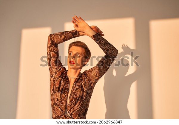Man with drag queen makeup holding his hands up
and looking away while
posing