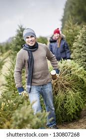Man dragging fresh spruce at cut your own Christmas tree farm with his daughter in background