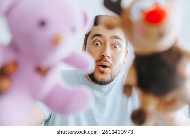 A man with a dramatic expression holding two plush toys up close to the camera, as if playing with a child, capturing a humorous and lighthearted moment.