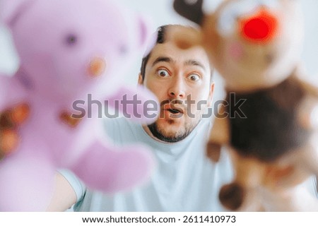 A man with a dramatic expression holding two plush toys up close to the camera, as if playing with a child, capturing a humorous and lighthearted moment.