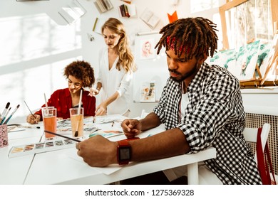 Man Drawing. Bearded Dark-haired Art Student With Dreadlocks Wearing Red Smart Watch Drawing