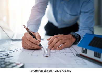 A man is drawing a house on a piece of paper with a pen. He is using a ruler to make sure the lines are straight. Concept of precision and attention to detail, as the man carefully draws the house - Powered by Shutterstock