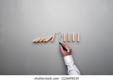 Man Drawing The Outline Of A Businessman Stopping The Domino Effect In A Conceptual Image On Gray Background.