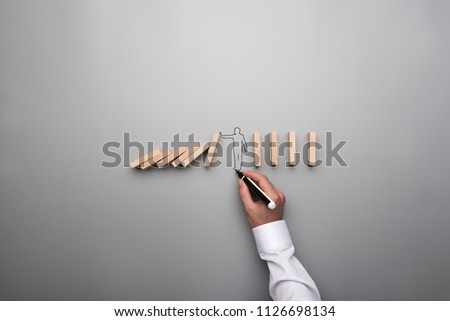 Man drawing the outline of a businessman stopping the domino effect in a conceptual image on gray background.