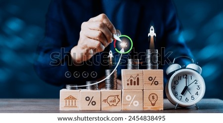 A man is drawing a rocket on a table with a clock and stacks of coins. The coins are arranged in a pyramid shape, with the top coin being the largest and the bottom one being the smallest