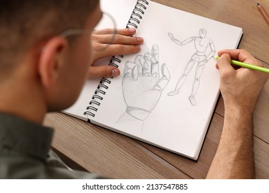 Man drawing in sketchbook and pencil at wooden table  closeup