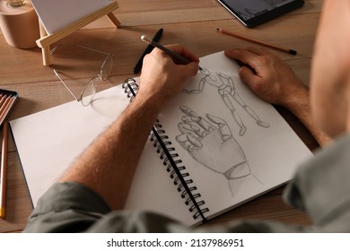 Man drawing in sketchbook with pencil at wooden table, closeup - Powered by Shutterstock