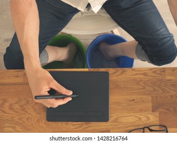 Man with drawing tablet at the desk, cools his feet in the water bucket