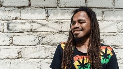A Man With Dreadlocks Against The Background Of The Wall Taken At Eye Level Looks A Little Sideways