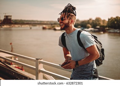 Man with dreadlocks and beard using phone by the river on a hot summer day - Powered by Shutterstock