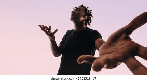 Man with dreadlocks dances energetically to music playing on his wireless earbuds. He showcases his unique dance moves in a studio, with his eyes closed and his hands in motion. - Powered by Shutterstock