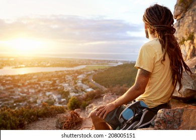 A man in dreadlocks on a mountain looking at the view with copyspace