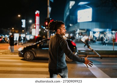Man with dreadlocks performing fire juggling on a city street at night, entertaining passersby with his show