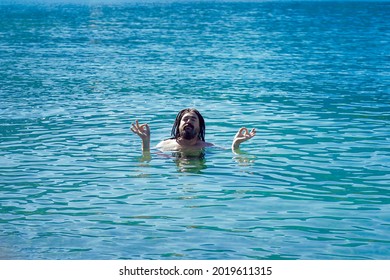 A man with dreadlocks in a relaxed Om position in turquoise water. Relaxation and enlightenment.