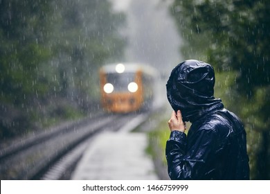 Man in drenched jacket standing on platform of railway station against train in heavy rain. - Powered by Shutterstock