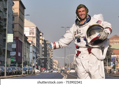 A man dressed as astronaut after losing hitchhiking on a city street. Concept of: adventure, hitchhiking, travel applications, surreal, space travel.