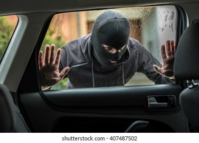 Man dressed in black with a balaclava on his head looking through car window and wondering how to break into this car. Car thief, car theft concept